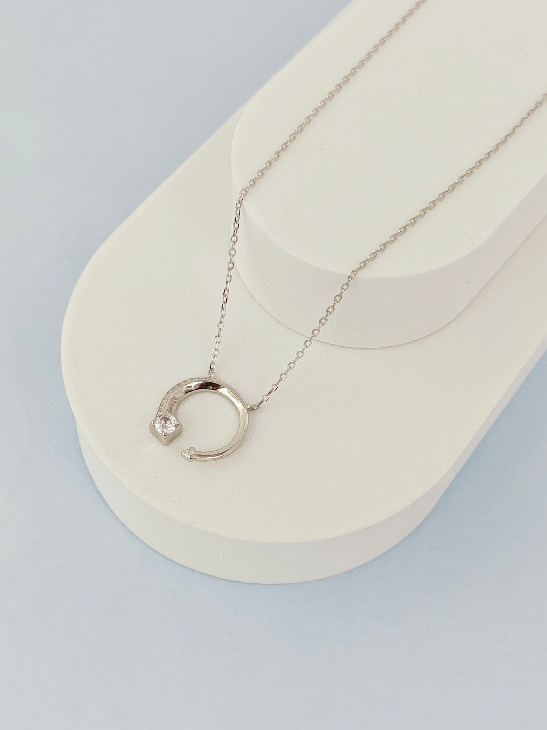 Silver necklace with a crescent moon pendant on a white stand against a light gray background